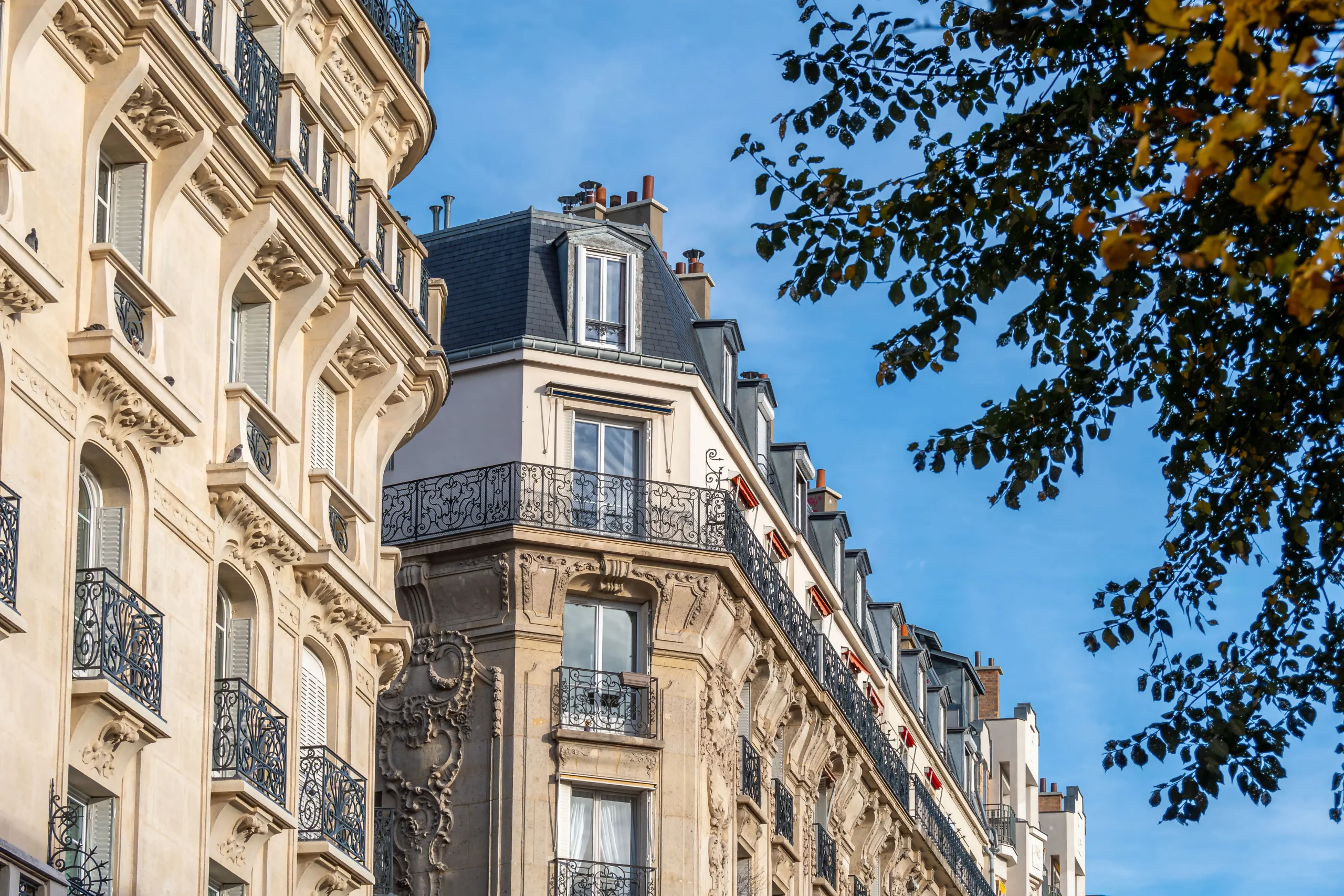 Immeuble ancien en ville vu depuis la rue, avec façades en pierre, balcons et ciel bleu en arrière-plan.